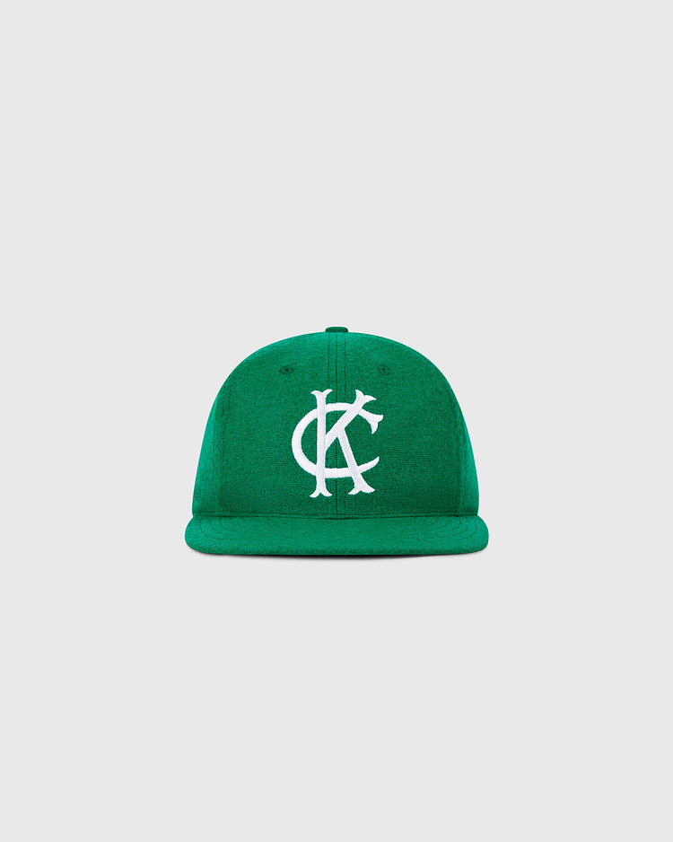 The Ebbets Field Kansas City Athletics 1963 MLB Authentic Wool Ballcap features a green flat brim and large white interlocking KC embroidery, inspired by the Decade of Change Collection. Shown on a plain light gray background.
