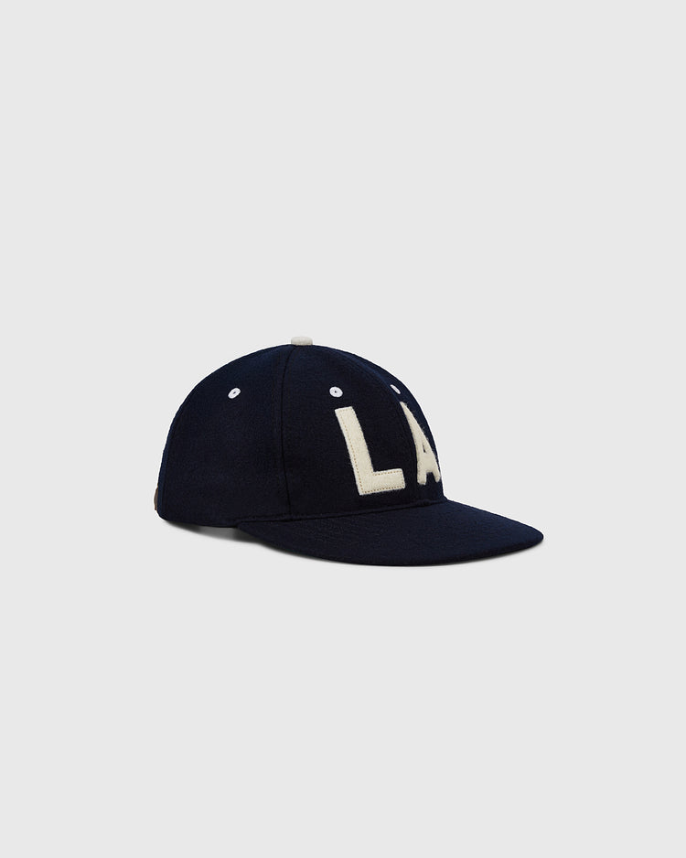 The EFF Los Angeles (PCL) 1954 Authentic Wool Ballcap is navy blue with a flat brim and bold white LA embroidery, inspired by the Pacific Coast League Angels, shown on a plain light gray background.