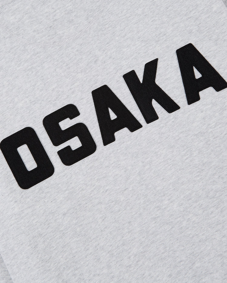 The image features the Osaka Tigers Heavyweight Cotton Terry Full-Zip Hoodie by Ebbets Field, showcasing “OSAKA” in bold black uppercase letters on a light gray fabric, giving it a vintage-inspired look.