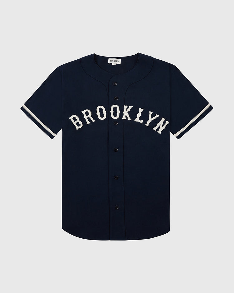 The Ebbets Field Brooklyn Eagles Cotton Twill Baseball Jersey is a navy short-sleeve top with white sleeve stripes, bold BROOKLYN lettering, and black front buttons, inspired by the Negro Leagues’ Brooklyn Eagles.