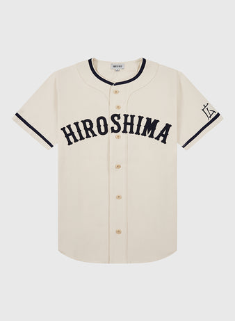 The Ebbets Field Hiroshima Carp Cotton Twill Baseball Jersey features cream cotton twill, “HIROSHIMA” in bold black on the chest, black sleeve trim, a left-sleeve graphic, and a classic button-down front.