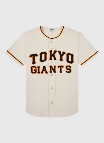 The Ebbets Field Tokyo Giants 1953 Cotton Twill Baseball Jersey features a cream color, short sleeves, bold black and orange “TOKYO GIANTS” lettering, orange and black collar and sleeve trim, and button closures down the front.