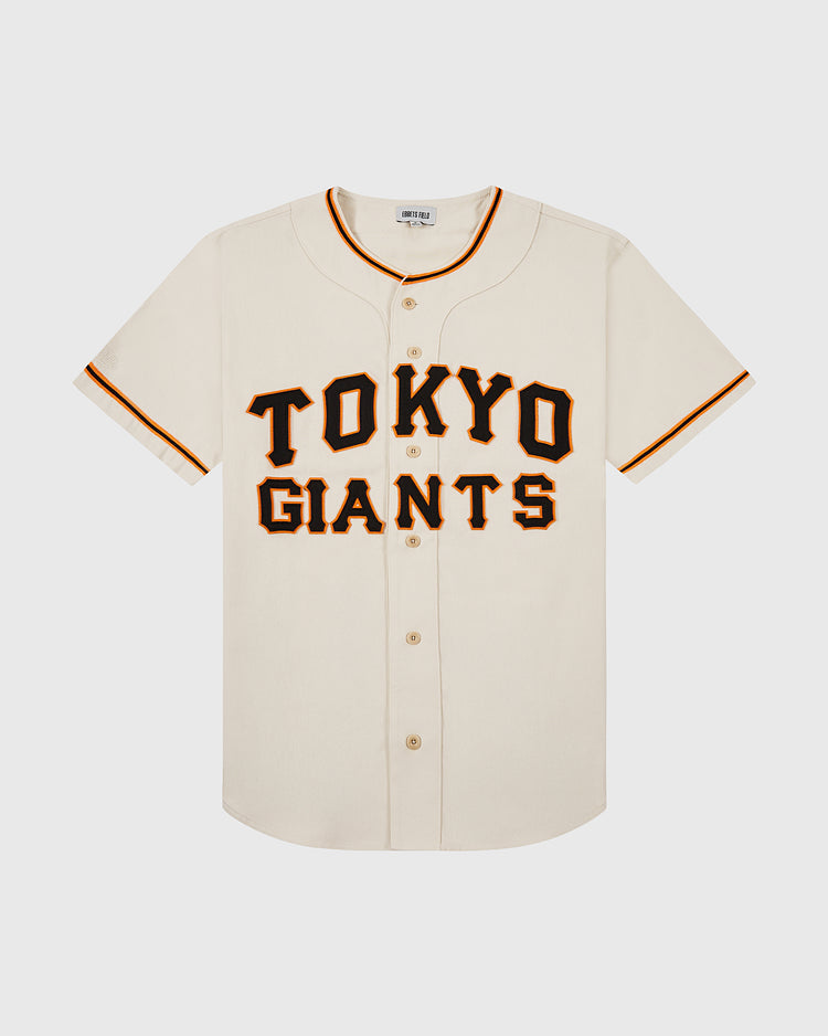 The Ebbets Field Tokyo Giants 1953 Cotton Twill Baseball Jersey features a cream color, short sleeves, bold black and orange “TOKYO GIANTS” lettering, orange and black collar and sleeve trim, and button closures down the front.