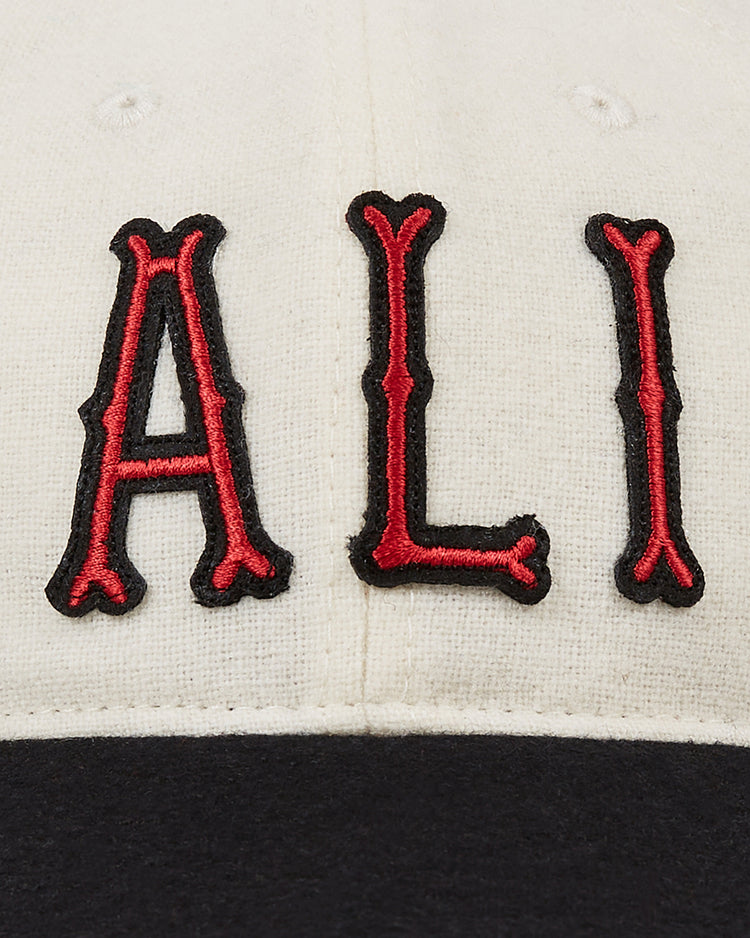 Close-up of the cream Muhammad Ali Vintage Inspired Wool Ballcap by Ebbets Field, featuring ALI boldly embroidered in red and black above a black brim—a homage to his