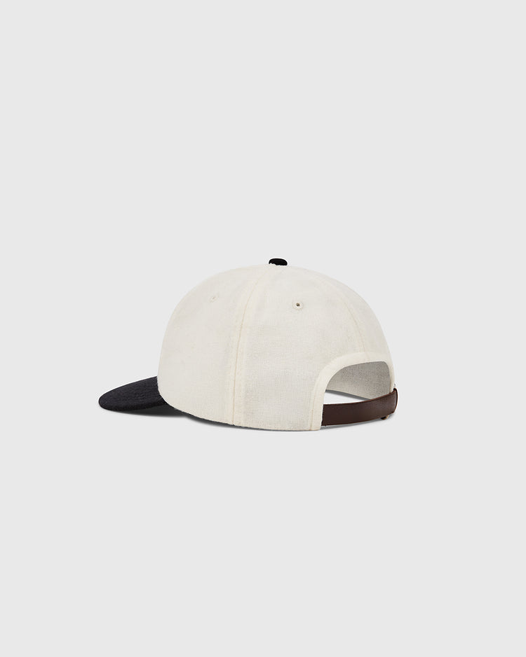 The Muhammad Ali Vintage Inspired Wool Ballcap by Ebbets Field features a cream crown, black bill, and brown adjustable strap with metal buckle. Its genuine wool nods to classic style, shown on a plain light gray background.
