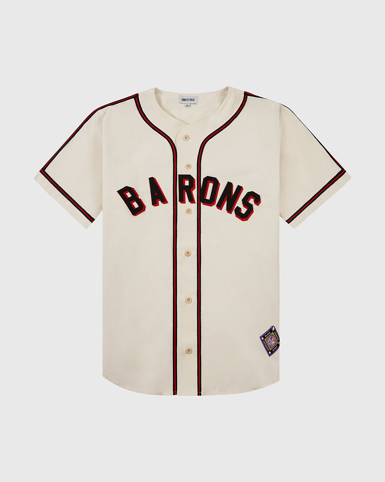 The Ebbets Field Birmingham Black Barons Cotton Twill Jersey features a cream color with black and red trim, black BARONS lettering across the chest, and a patch near the hem, honoring legends like Satchel Paige and Willie Mays.