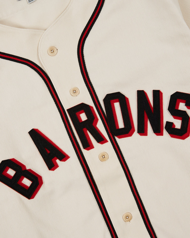 The Ebbets Field Birmingham Black Barons Cotton Twill Jersey features cream cotton twill, black and red trim, “BARONS” in black with red outline across the chest, and beige buttons, honoring the legendary team of Satchel Paige and Willie Mays.