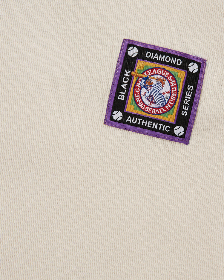 The Birmingham Black Barons Cotton Twill Jersey by Ebbets Field features beige fabric with a colorful patch displaying BLACK DIAMOND SERIES, AUTHENTIC text, baseball icons, and a central graphic—honoring legends like Willie Mays.