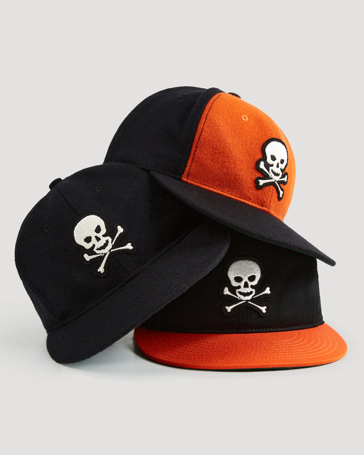 Three Ebbets Field vintage wool ballcaps—including a Sioux City Ghosts design—are stacked together: two are black with white embroidery and one has black and orange accents, all set on a plain background.