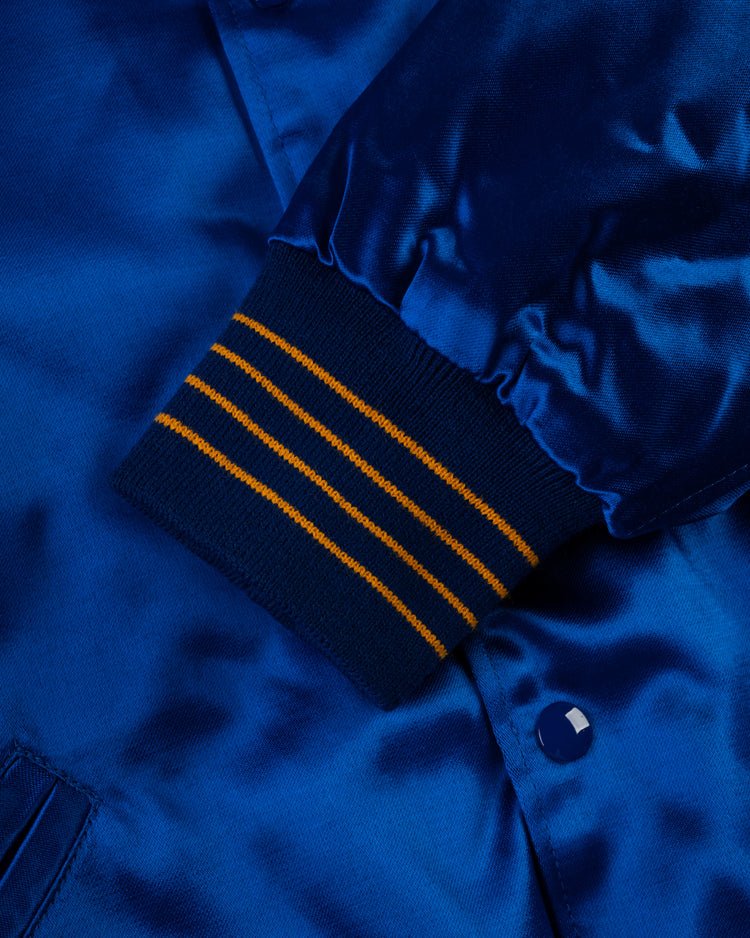 Close-up of the shiny blue satin Seattle Pilots 1969 Authentic All Satin Varsity Jacket by EFF, showing a ribbed dark blue cuff with three yellow stripes, plus part of a blue button and pocket—a true replica detail.