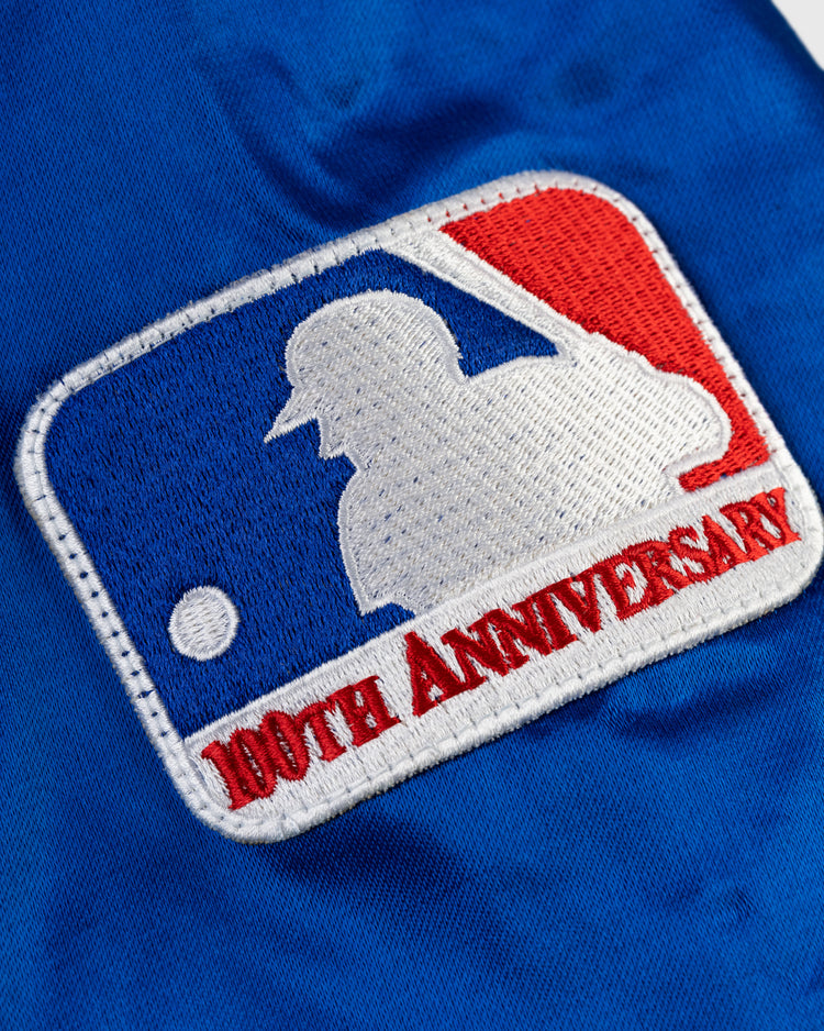 Close-up of a patch with the Major League Baseball logo and 100th Anniversary in red, on blue satin fabric from the EFF Seattle Pilots 1969 Authentic All Satin Varsity Jacket.