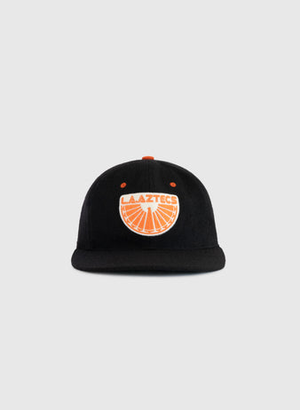 The EFF Los Angeles Aztecs 1976 Authentic Wool Ballcap is a black cap with an orange button and an orange and white LA Aztecs logo featuring a soccer ball, honoring NASL soccer history, shown on a plain light gray background.