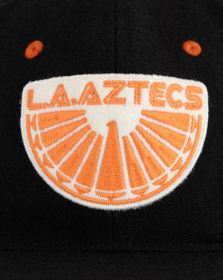 The EFF Los Angeles Aztecs 1976 Authentic Wool Ballcap is a black cap with an orange and white LA Aztecs patch above a sun-inspired design—perfect for classic American soccer and NASL fans.