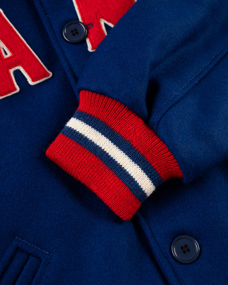 Close-up of the EFF New York Giants 1932 Authentic All Wool Varsity Jacket, featuring blue wool, navy blue buttons, red, white, and blue striped ribbed cuffs, and a partial red and white letter patch on the chest.