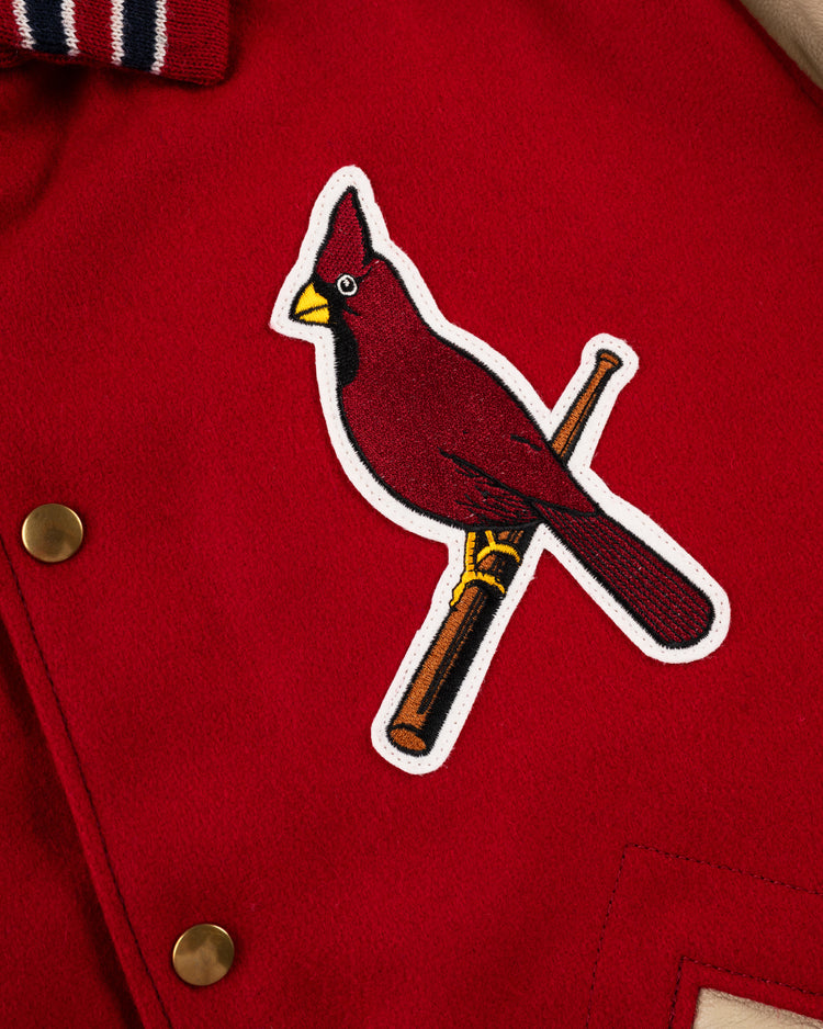A close-up of the EFF St. Louis Cardinals 1940 Authentic Wool & Leather Jacket, featuring gold buttons and a patch of a cardinal on a yellow bat. The red jacket has a red, white, and blue striped collar.
