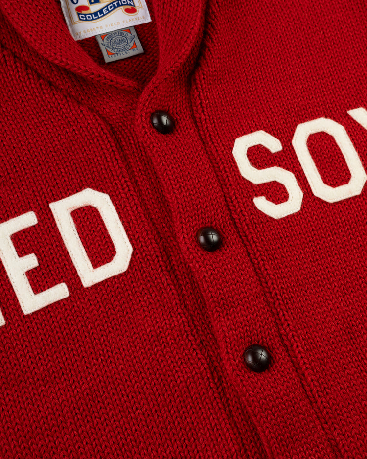 Close-up of the EFF Boston Red Sox 1917 Wool Shawl Collar Sweater featuring red knit fabric, white RED SOX lettering, black buttons, and a visible Cooperstown Collection label—recalling Babe Ruth’s iconic Dead Ball Era team.