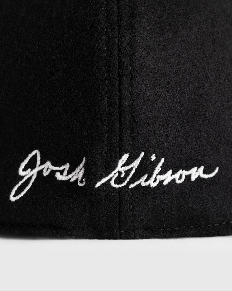 Close-up of black wool ballcap by Ebbets Field Flannels, featuring white embroidered cursive Josh Gibson—a tribute to the legendary Negro Leagues star. Part of the 1945 Signature Series.