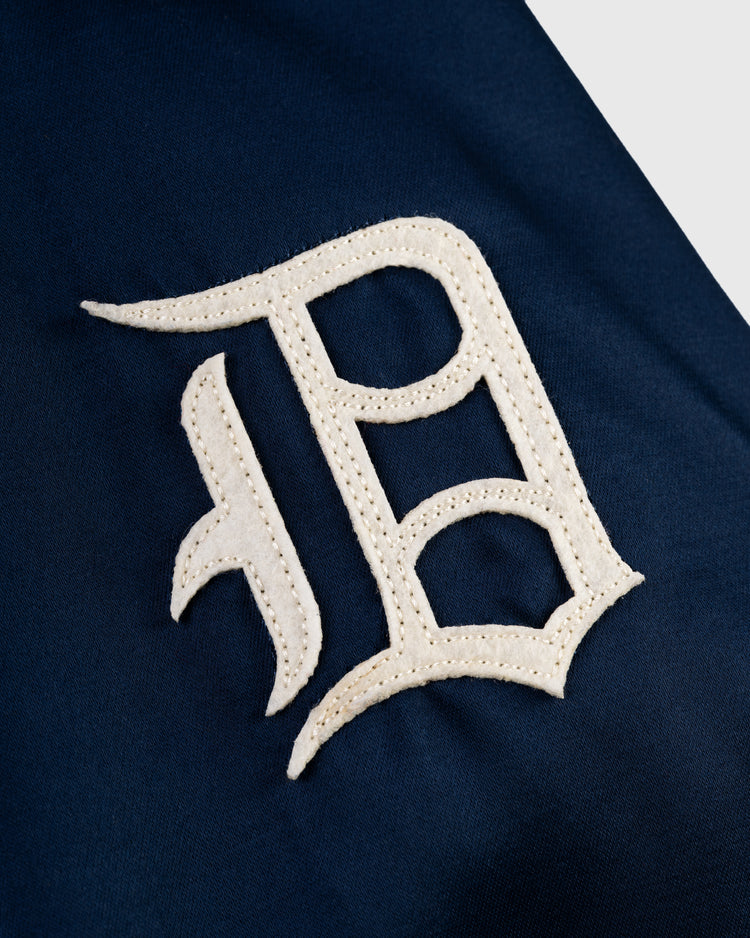 Close-up of a white, old English-style D patch sewn on navy blue fabric, inspired by the Detroit Tigers 1960 Satin Windbreaker Jacket from EFF for a classic MLB vintage look.