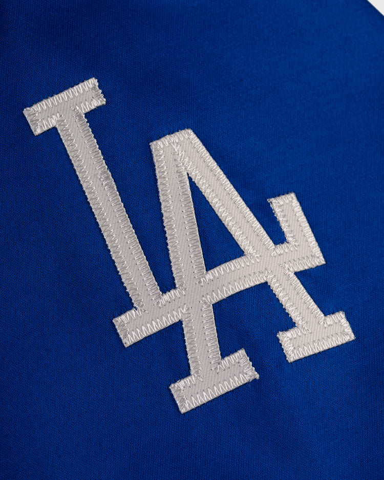White LA logo stitched on blue fabric, inspired by the iconic Los Angeles Dodgers 1962 Satin Windbreaker Jacket by EFF, representing the team at Dodger Stadium.