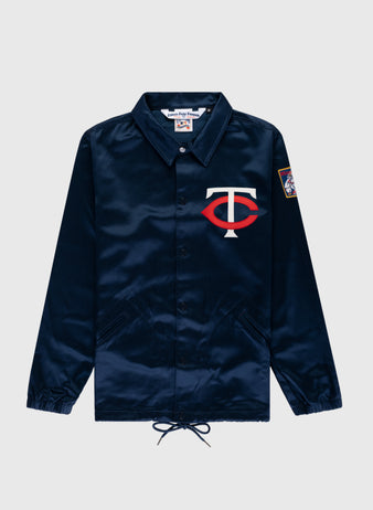 The EFF Minnesota Twins 1966 Satin Windbreaker Jacket is navy blue with a white and red TC logo on the left chest and a colorful patch on the right sleeve, shown against a light gray background.