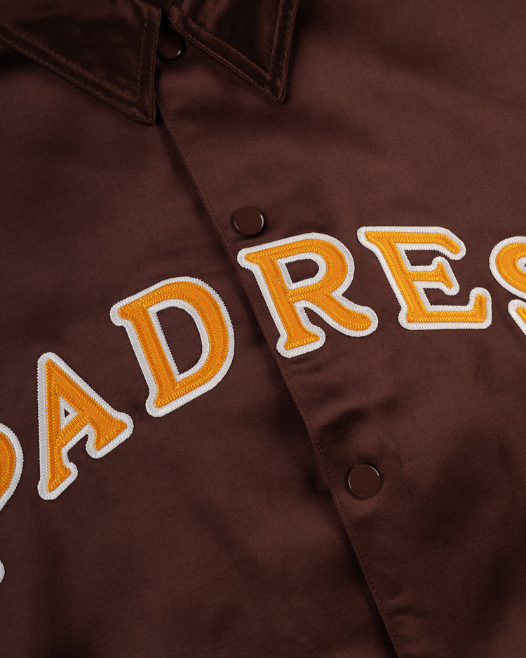 Close-up of the EFF San Diego Padres 1969 Satin Windbreaker Jacket in brown, featuring large yellow and white embroidery, snap buttons, and a collar—a classic MLB vintage-inspired design.