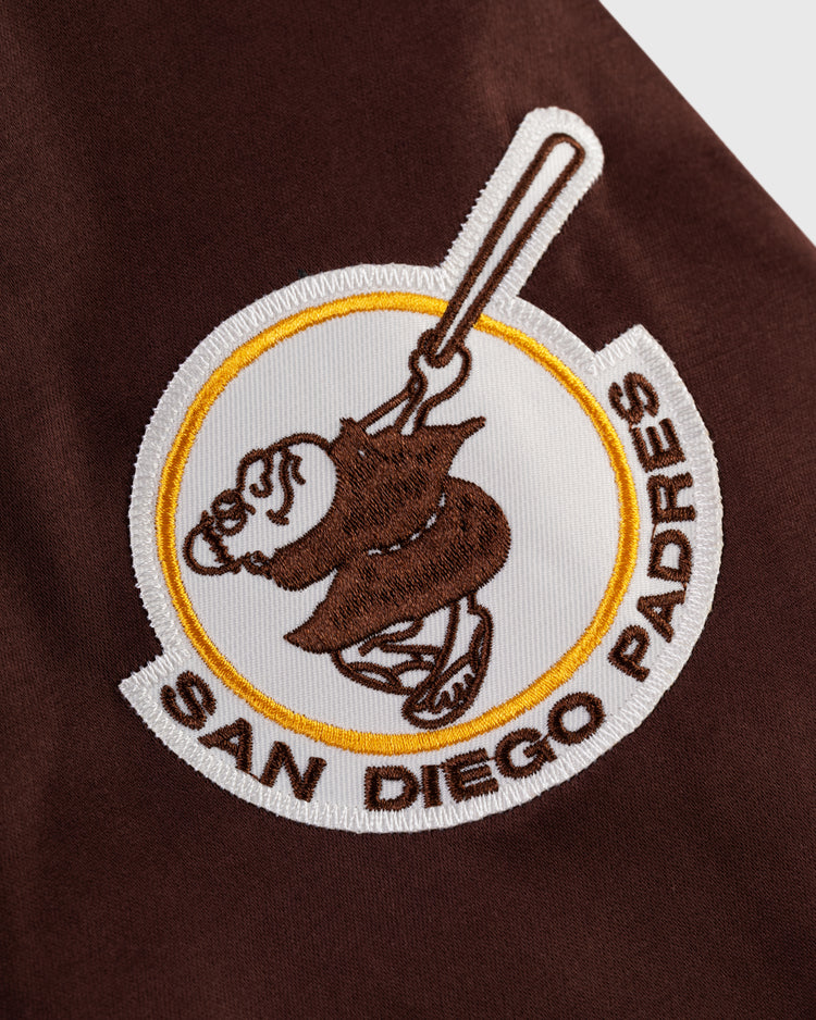 A brown and white embroidered patch with a friar swinging a bat and SAN DIEGO PADRES in brown is sewn onto the EFF San Diego Padres 1969 Satin Windbreaker Jacket, made from classic brown fabric.