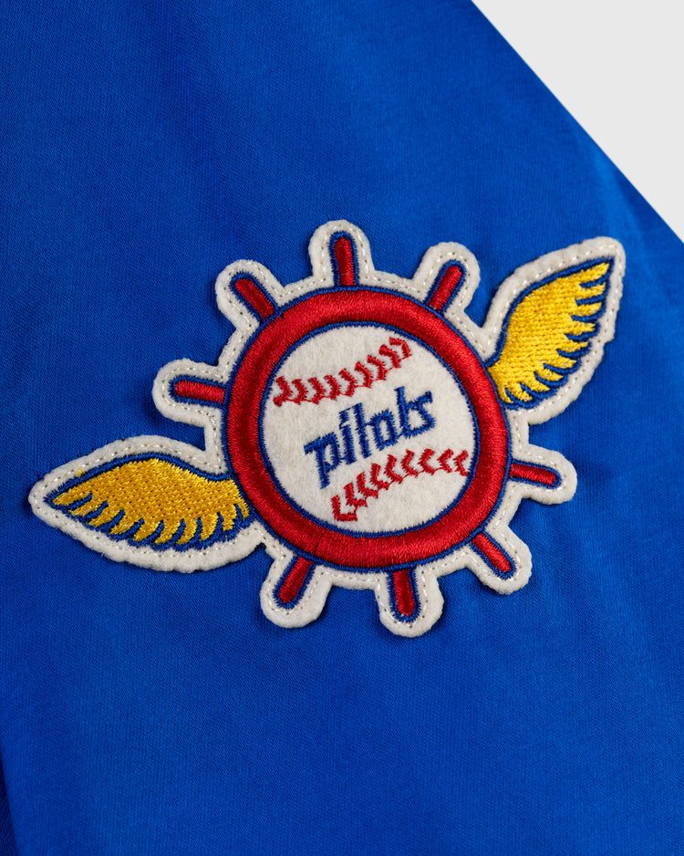 An embroidered patch featuring a baseball with red stitching, yellow wings, and pilots in blue script is sewn onto blue fabric on the EFF Seattle Pilots 1969 Satin Windbreaker Jacket.