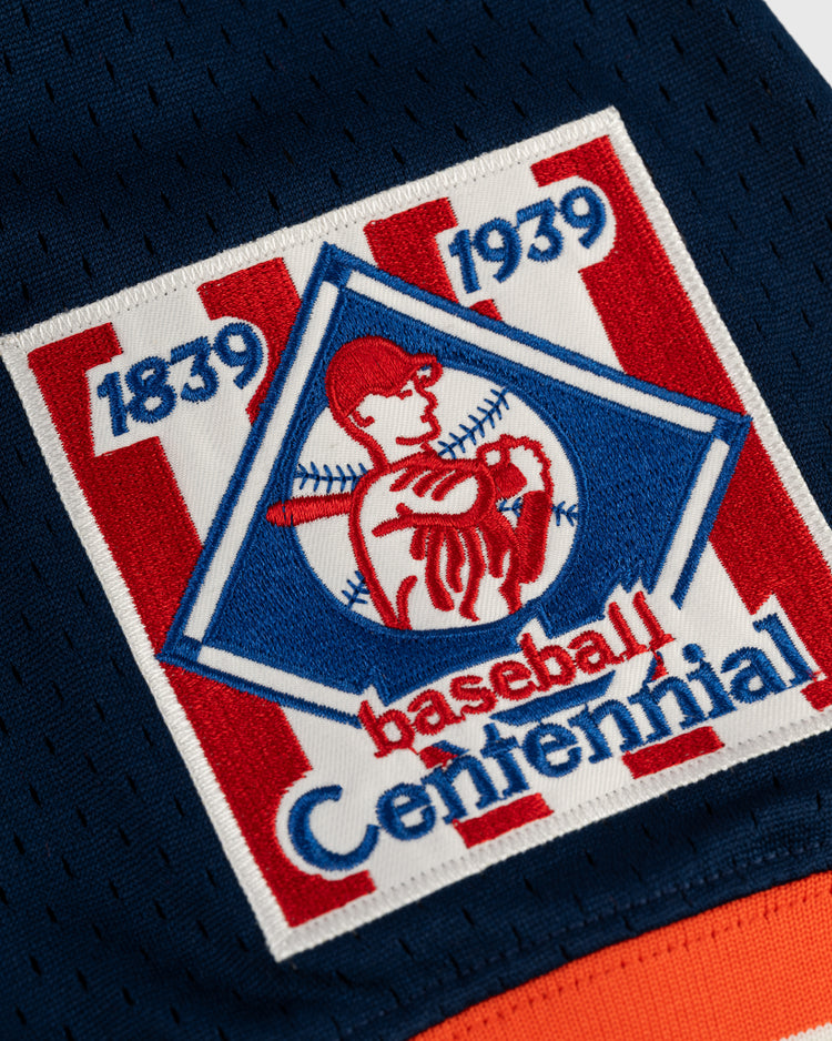 A close-up of a patch with red and white stripes, blue border, and baseball player reading “1839 1939 Baseball Centennial,” sewn onto dark blue fabric—a classic detail on the EFF New York Knights Mesh V-Neck Jersey.