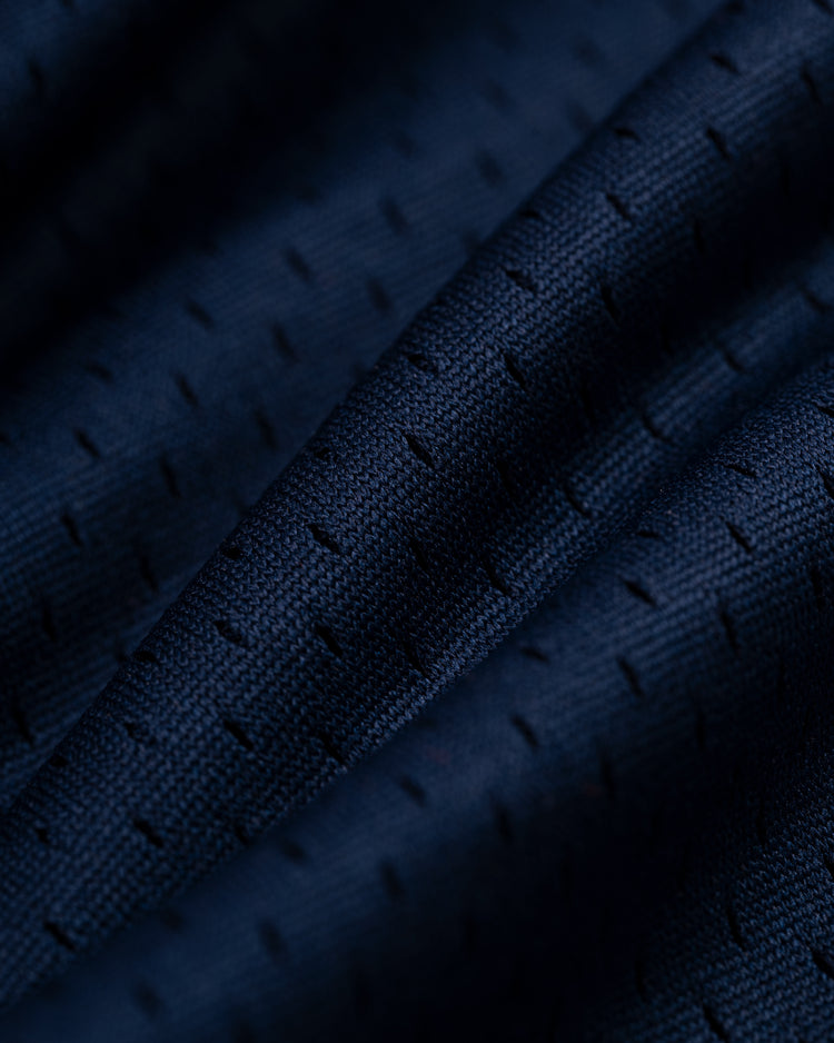 Close-up of dark blue textured fabric with small, evenly spaced perforations and gentle folds, evoking a vintage style like the EFF New York Knights Mesh V-Neck Jersey.