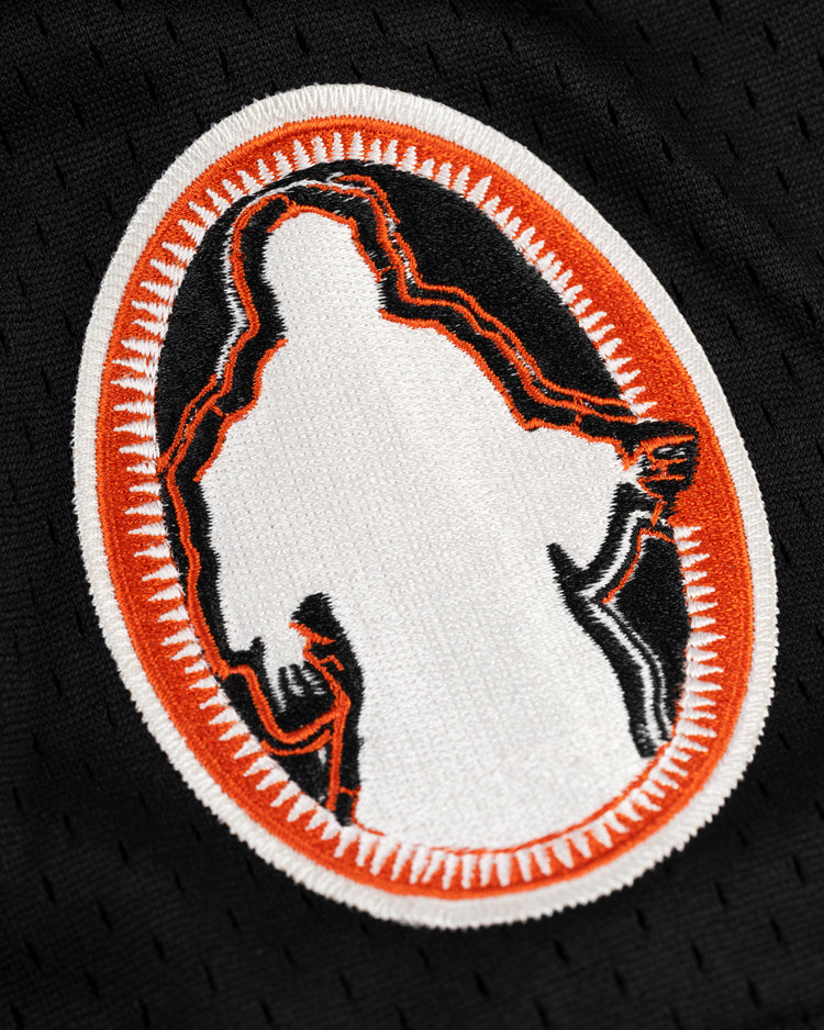 The EFF Sioux City Ghosts Mesh Button-Up Jersey features an embroidered patch with a white silhouette outlined in orange and black, honoring the historic barnstorming softball team, set on black fabric with an oval orange and white border.