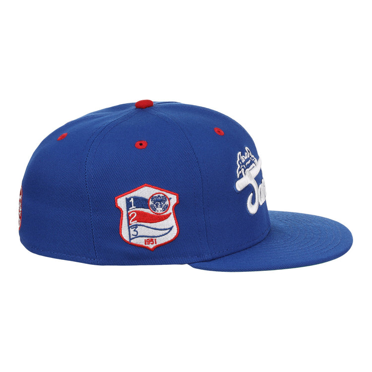The EFF Santurce Cangrejeros NLB Team Color Fitted Ballcap is a blue vintage-style cap with a flat brim, side white embroidered logo, and a red, white & blue Puerto Rican League patch featuring numbers and shield on the front side panel.