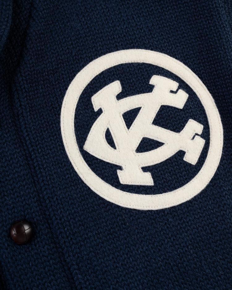 Close-up of the EFF Kansas City Monarchs 1922 Wool Shawl Collar Sweater in navy, featuring a white patch with overlapping V and C letters—a nod to classic Negro Leagues World Series styles. Black button visible on the left.