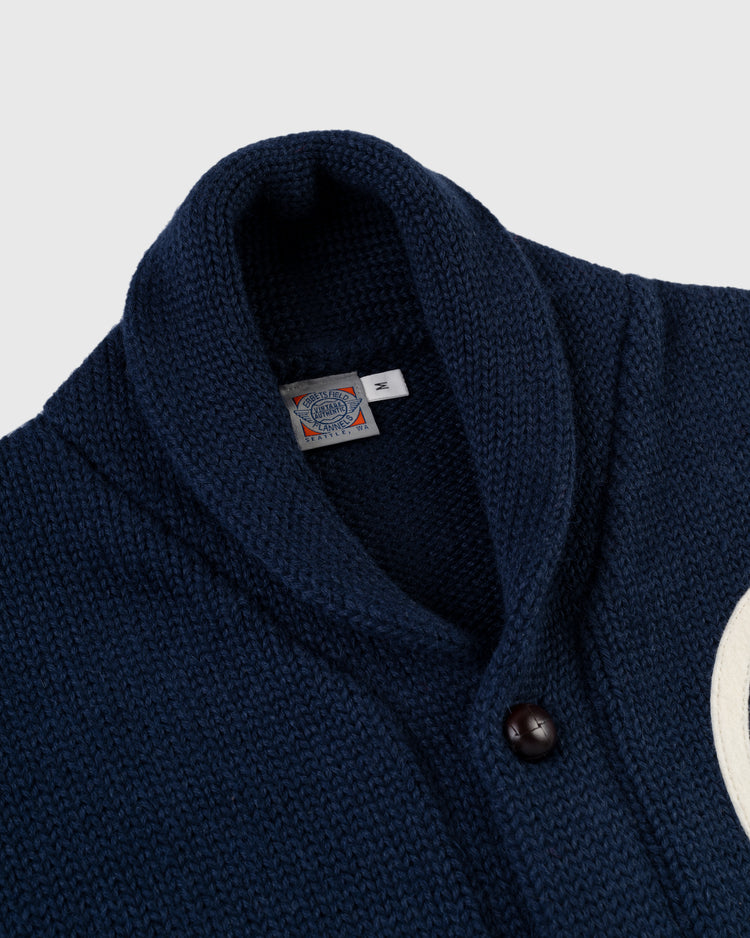 A close-up of the EFF Kansas City Monarchs 1922 Wool Shawl Collar Sweater in navy, featuring a button and visible M-labeled neck tag; part of a white patch appears on the right side.
