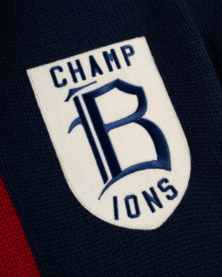 The EFF Boston Braves 1915 Wool Shawl Collar Sweater features a shield-shaped patch with CHAMPIONS split by a large blue B on white, set against the sweaters dark blue and red design.