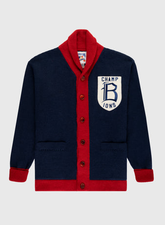 The EFF Boston Braves 1915 Wool Shawl Collar Sweater is a navy blue cardigan with red trim and buttons, featuring a large white CHAMPIONS patch and stylized B on the left chest, inspired by the classic 1915 design.