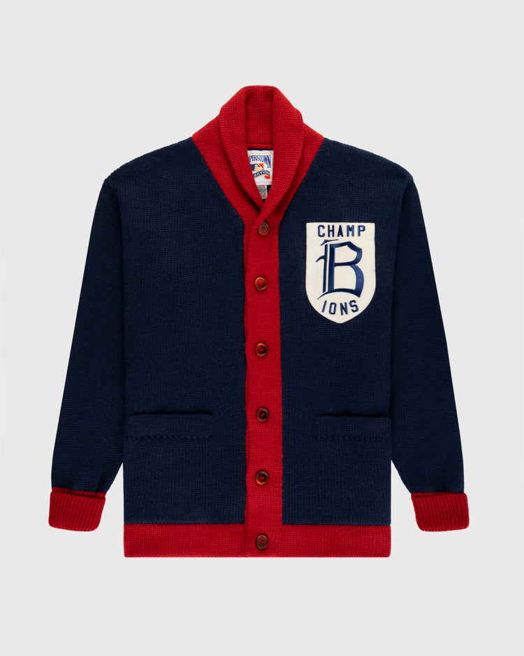 The EFF Boston Braves 1915 Wool Shawl Collar Sweater is a navy blue cardigan with red trim and buttons, featuring a large white CHAMPIONS patch and stylized B on the left chest, inspired by the classic 1915 design.