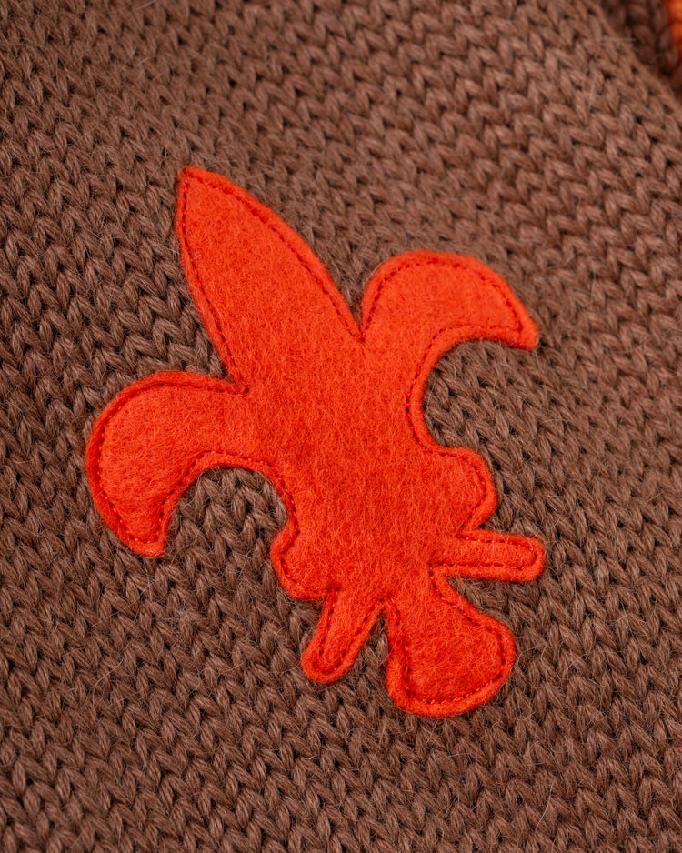 Close-up of an orange felt fleur-de-lis sewn onto brown knit fabric, inspired by the EFF St. Louis Browns 1909 Wool Cardigan Sweater, similar to the one worn by legends like Rube Waddell.