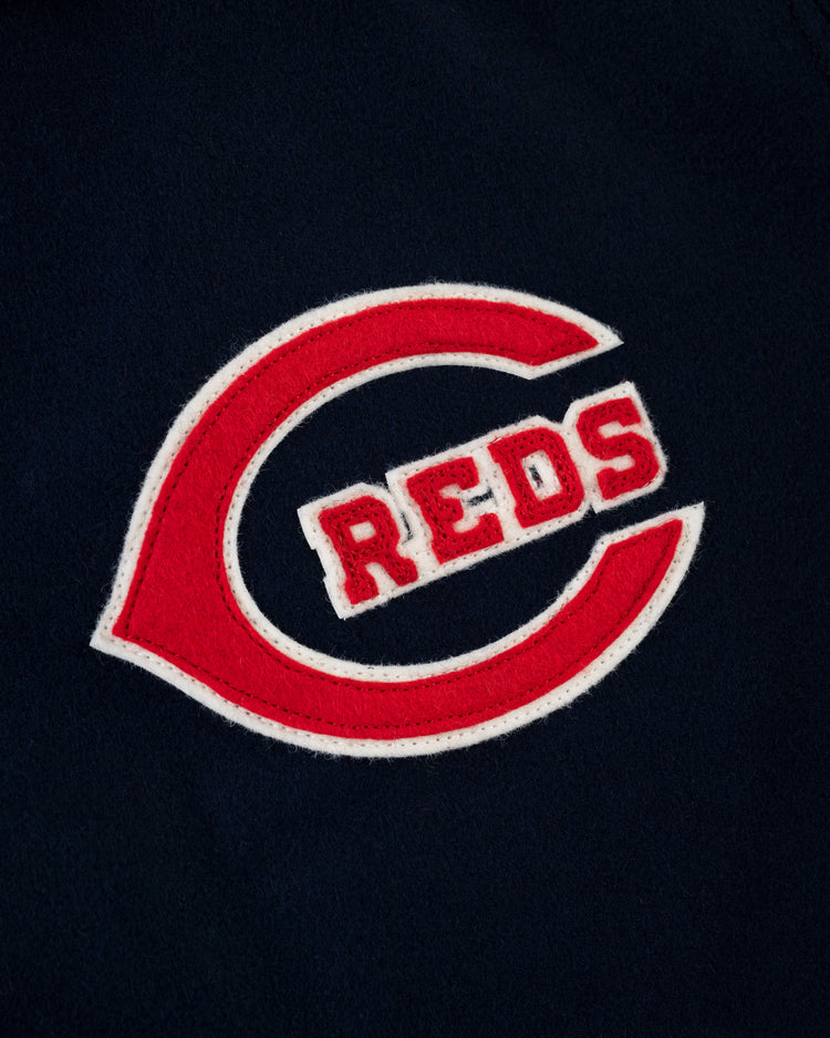 A close-up of the EFF Cincinnati Reds 1942 Authentic All Wool Varsity Jacket shows a red letter C patch with REDS inside, outlined in white on a dark blue wool background.