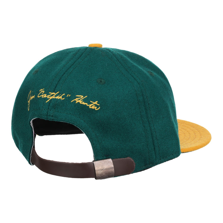 The Ebbets Field Flannels Catfish Hunter Signature Series Ballcap features vintage green wool, a yellow brim and button, yellow script embroidery on the back, and an adjustable brown strap with metal clasp.