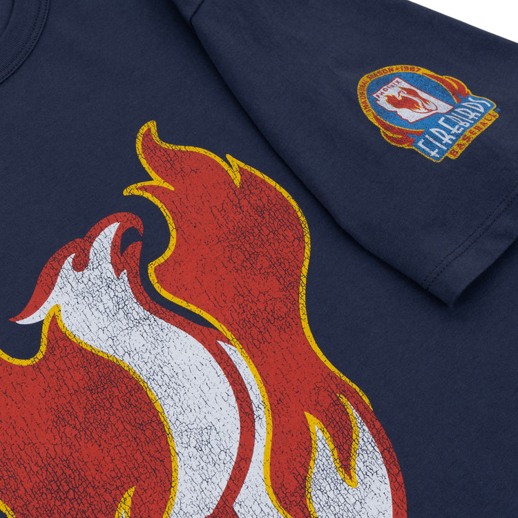 The Ebbets Field Flannels Phoenix Firebirds EFF MiLB Vintage T-Shirt features a navy blue design with a bold red and white flame graphic and a colorful Fireland patch on the sleeve, inspired by classic Minor League styles.