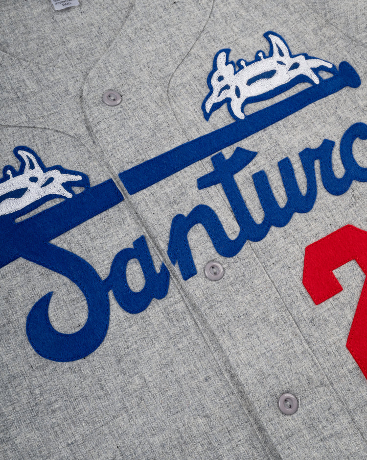 Close-up of the Ebbets Field Santurce Cangrejeros 1954 Authentic Wool Road Baseball Jersey, featuring grey wool, blue script Santurce with a white and blue crown, and a red partial number 2 inspired by Roberto Clemente.