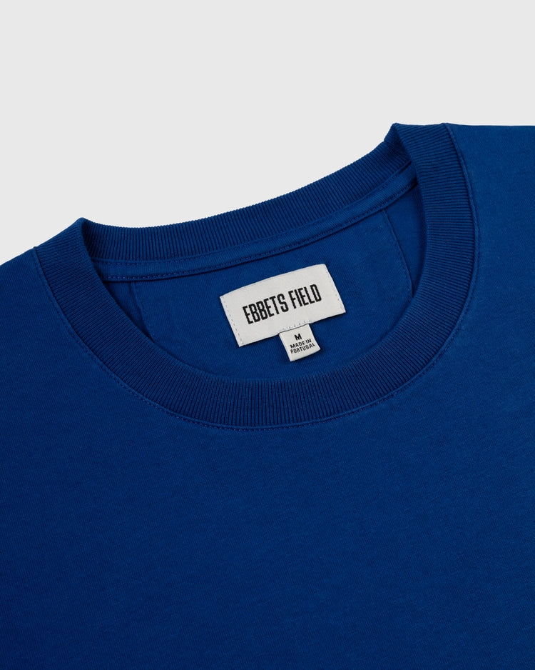 Close-up of a royal blue Ebbets Field Los Angeles Angels (PCL) ‘LA’ Short Sleeve Tee with a white collar tag reading EBBETS FIELD, a size M and Made in Korea tag below, inspired by the 1942 LA team logo.