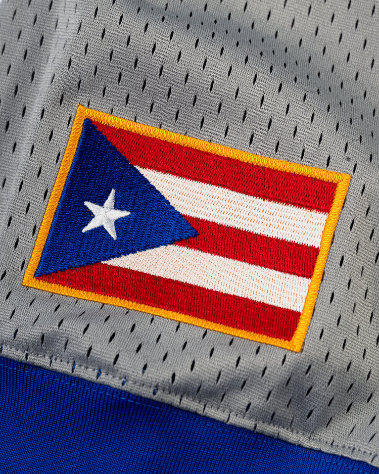 The Ebbets Field Puerto Rico 1958 National Team Mesh V-Neck Jersey features a gray perforated mesh build with a stitched Puerto Rican flag patch—yellow border, red and white stripes, blue triangle, and white star.