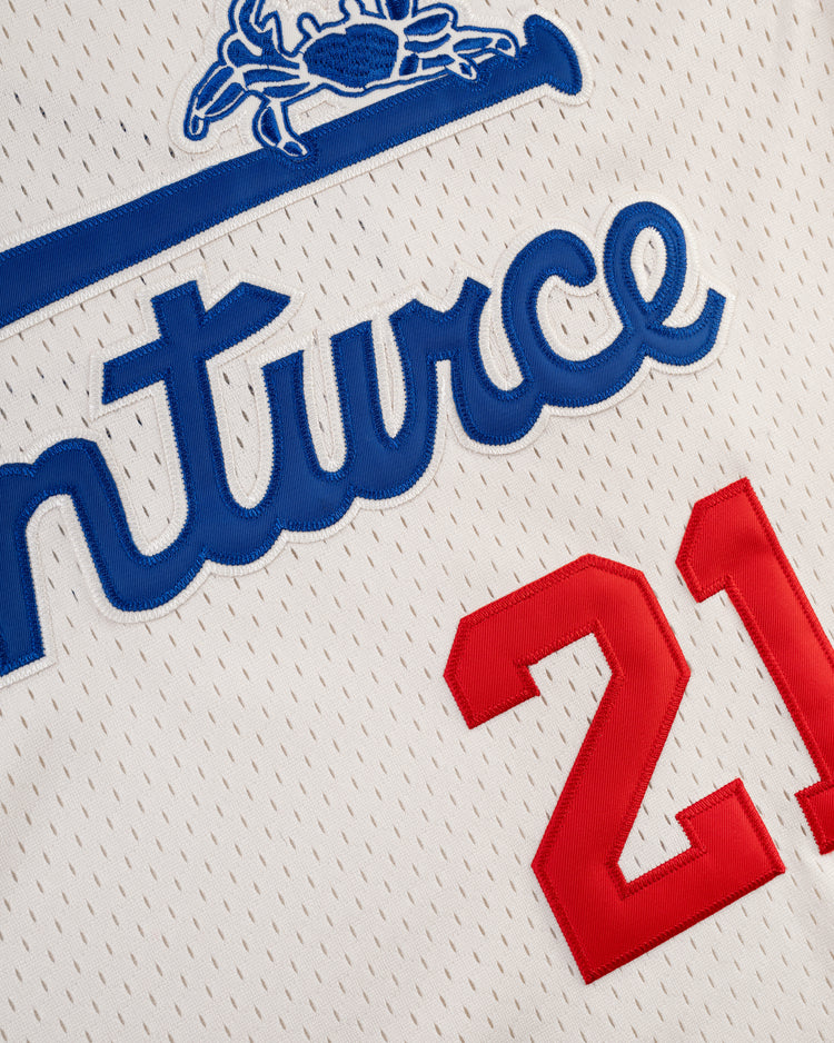 A close-up of the Santurce Cangrejeros Mesh V-Neck Jersey by Ebbets Field, featuring blue script lettering, part of a horse graphic above, and red number 21—a tribute to Puerto Rican baseball legend Roberto Clemente.