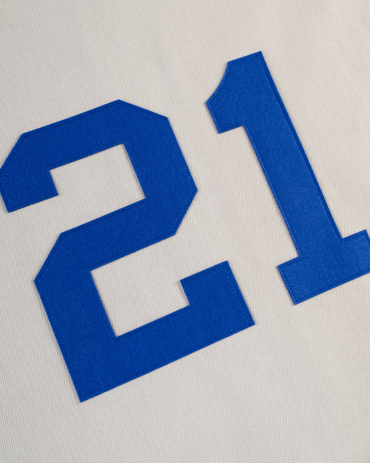 Large blue number 21 on white textured fabric, resembling the Puerto Rico 1958 National Team Cotton Twill Baseball Jersey by Ebbets Field.
