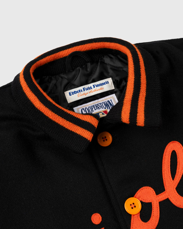 Close-up of a black EFF Baltimore Orioles 1966 Authentic All Wool Varsity Jacket with orange buttons, striped collar, and embroidered orange lettering; inside label shows Ebbets Field Flannels and Cooperstown Collection.