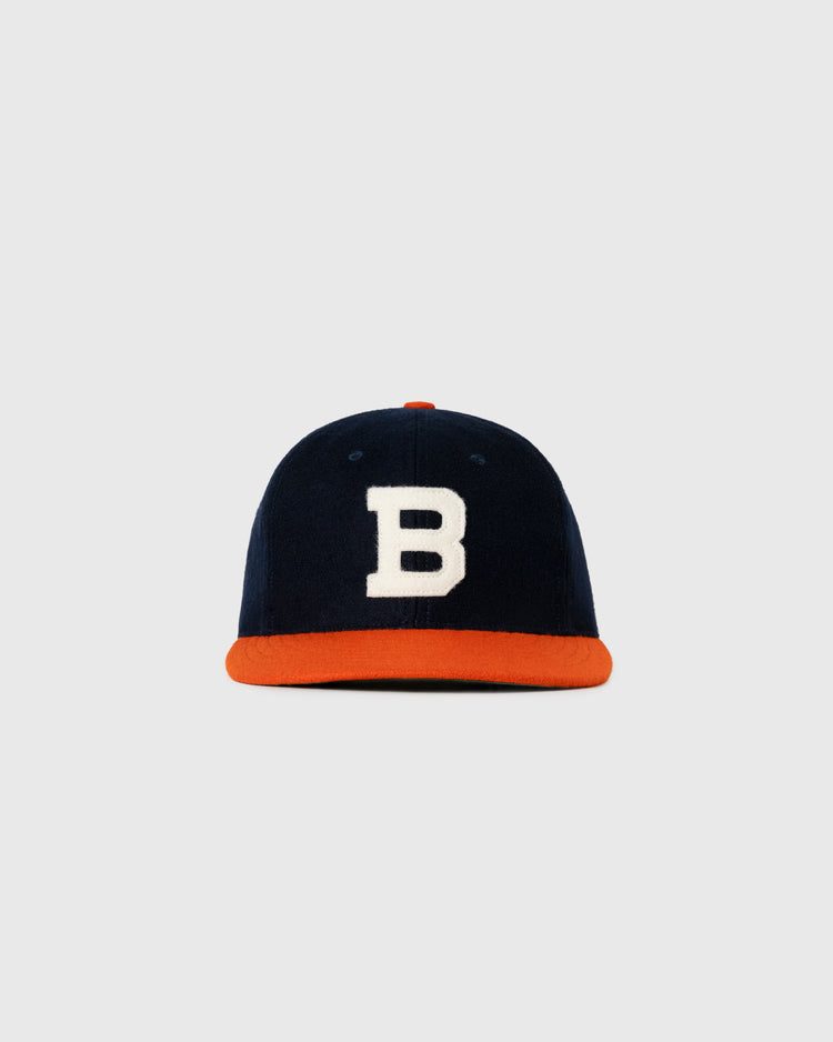 The EFF Brooklyn Bushwicks 1949 Authentic Wool Ballcap features navy blue wool, a white B on the front, and an orange brim, inspired by the original cap and shown against a plain light gray background.