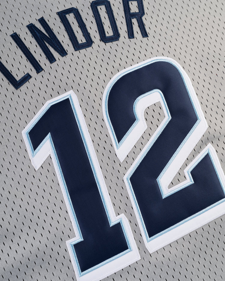 A close-up of the FRANCISCO LINDOR BUTTON UP MESH JERSEY GRY by Ebbets Field, showcasing Lindor and the number 12 in bold dark blue letters with white outlines on a gray sports jersey.