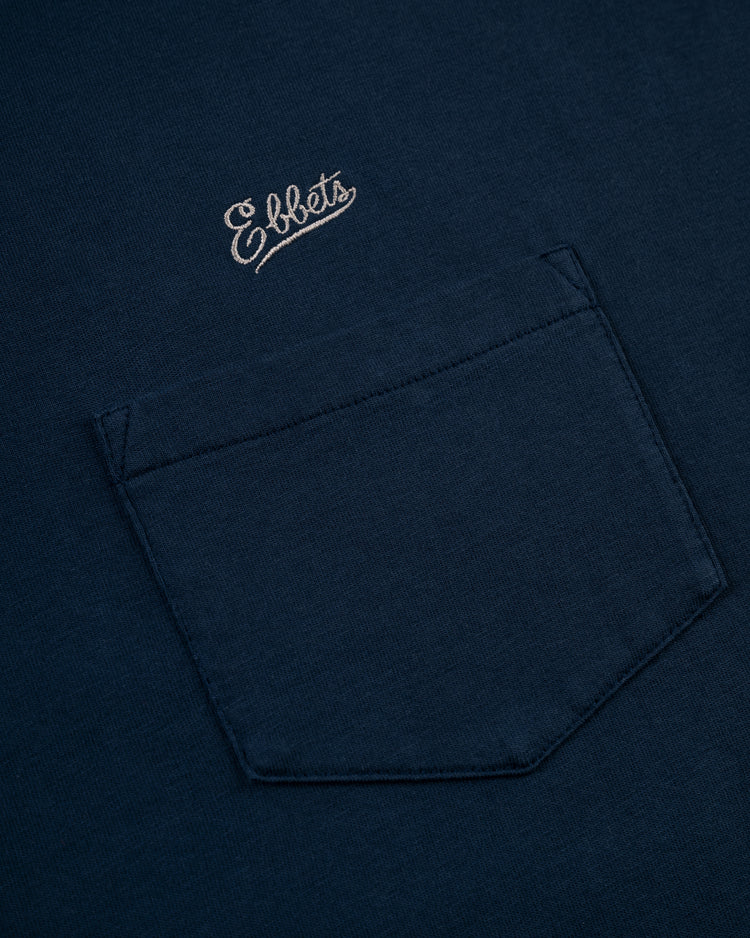 Close-up of the Ebbets Field Flannels Ebbets Chest Logo Long Sleeve Pocket Tee in navy, featuring a white embroidered Ebbets logo above the pocket—a classic, timeless addition to any wardrobe.