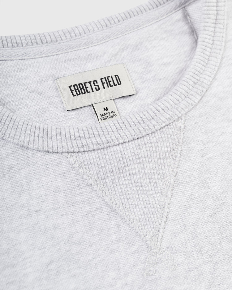 Close-up of the Ebbets Field Flannels Ebbets Chest Logo Heavyweight Cotton Terry Crewneck in light gray, featuring a ribbed collar with stitched V detail and two labels, M Made in Portugal. Crafted from heavyweight cotton for comfort and timeless style.